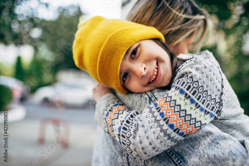 Candid portrait of a happy little girl in the yellow hat hugging her mom. Happy kid embracing her mother enjoying the time together outside. Joyful mom and daughter share love. Mother's day