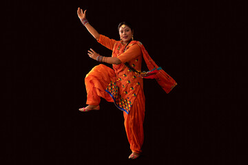 A woman in Giddha costume depicting a dance step with hands and a leg in the air.	 - obrazy, fototapety, plakaty