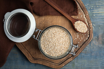 Jar and spoon with white quinoa on blue wooden table, flat lay