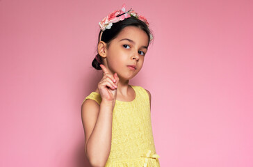 Studio portrait of a little girl wearing a yellow dress pointing with forefinger up for advertising text. Child pointing up with finger for attention posing on pink background.