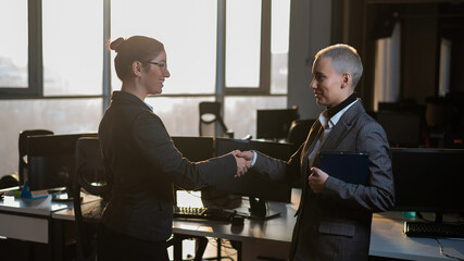 Two young business women shake hands at work. The office staff made a deal