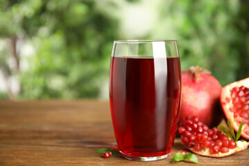 Pomegranate juice in glass and fresh fruits on wooden table outdoors, space for text