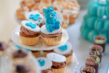 Adorable cupcakes with blue royal icing bear figurines and chocolate cream, sweet treats set on tiered white plates and prepared for a delicious desert bar at a baby shower or a child's birthday party