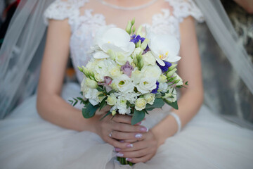 Beautiful bride wearing a gorgeous white dress and veil while holding a beautiful bouquet, delicate floral arrangement with orchids, roses and blue accents, a traditional accessory for the wedding day