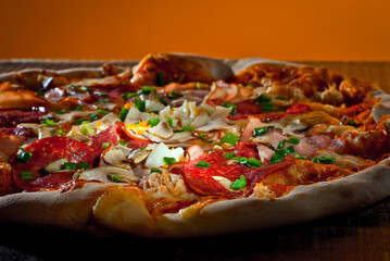 Round pizza on a wooden board. Pizza on a black table close up. Contrasting dramatic light as an artistic effect.