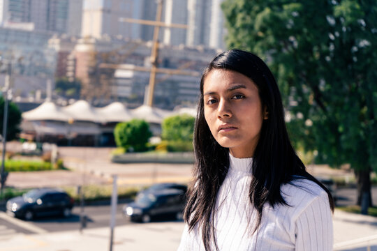 Mid-shot Portrait Of A Serious Black-haired Latina Woman With The City In The Background.