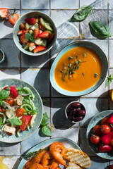 Mediterranean dishes at tiles table: seafood shrimps, vegetable salad, pumpkin soup, seeds and fruit lemonade