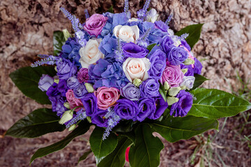 Beautiful bouquet with purple tones, exquisite floral arrangement, centerpiece or a bridal accessory inspiration featuring colorful roses, blue hydrangeas and greenery set against a natural background