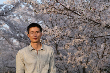 mid shot of one smiling Asian young man under sunshine with white sakura flower tree