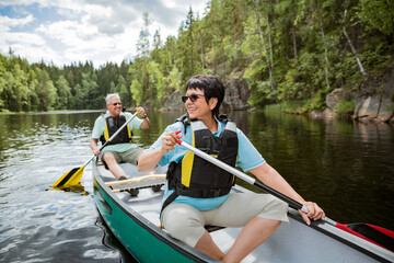 Happy mature couple in life vests canoeing in forest lake. Sunny summer day. Tourists traveling in...