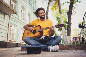 Fototapeta na wymiar Photo portrait of young man performing on guitar sitting on street in summer near black hat for money