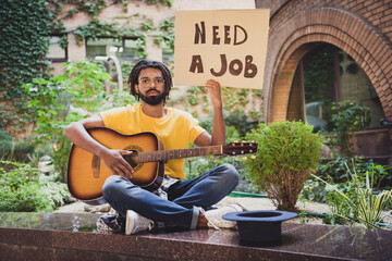 Obraz premium Photo portrait of jobless sad grumpy guy need money showing carton looking for work sitting on street keeping guitar with hat