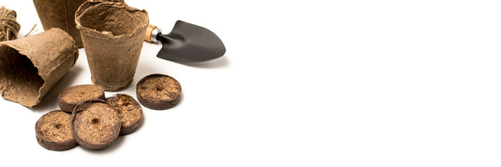 Biodegradable peat pots, seedling planting tools and pressed ground on white background with copy space. The concept of growing food, plant on the windowsill and in the greenhouse