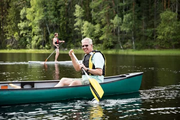 Foto op Canvas Happy mature couple in life vests canoeing in forest lake. Sunny summer day. Tourists traveling in Finland, having adventure.  © Suzi Media 