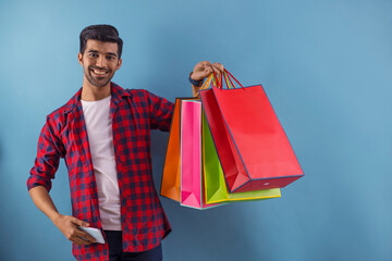 A young man standing with carry bags and a mobile in his hands.	