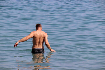 Muscular man going to swim in sea water, back view. Beach vacation and swimming