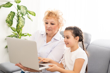 modern grandmother teaching grandchild how to use laptop computer at home