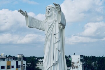 Jesus statue standing and blessing with both the hands against blue sky background.