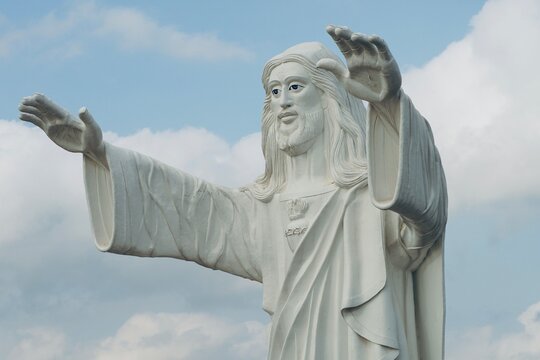 Jesus statue standing and blessing with both the hands against blue sky background.