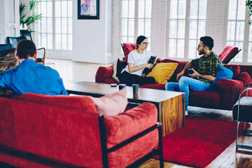 Young people with coffee to go in hands have socialising conversation in apartment with modern interior, diverse hipster guys talking spending leisure time for gathering at home loft interior