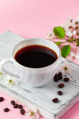 Strong espresso coffee on a white wooden tray. Spring flowers of an apple tree on a pink background. Good morning and spring time concept.