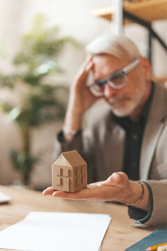 Inheritance problems. An elderly man holds a model at home and grabs his head. Real estate crisis, mortgage payments.