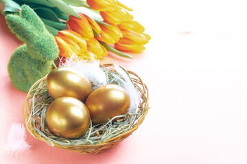 Easter eggs Golden color in basket with spring tulips, white feathers on pastel pink background in Happy Easter decoration. Festive decoration.