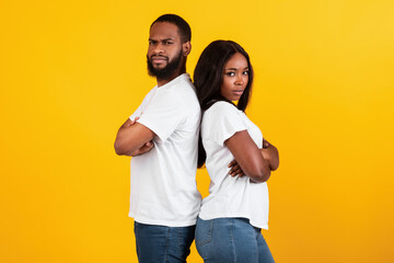 Afro couple standing back to back, yellow studio background