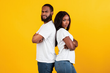 Obraz premium Afro couple standing back to back, yellow studio background