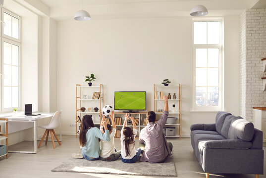 Football match, leisure and happy family sport fan pastime together. Excited parent with overjoyed children watching soccer game on tv sitting on floor carpet in living room at home. Rear view