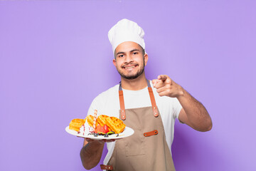 young hispanic man pointing or showing. chef with waffles concept