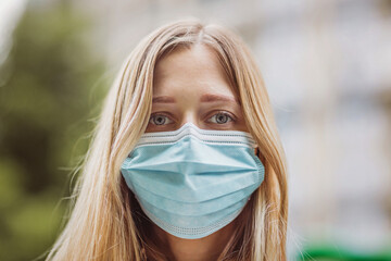 Young caucasian woman with blonde hair protective face mask. Close up portrait. Vogue, street style during quarantine coronavirus covid-19 outbreak.