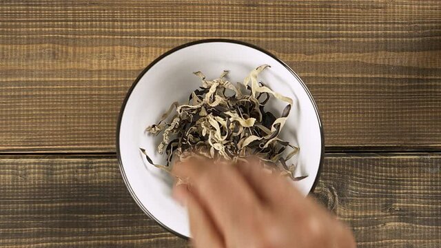 A man's hand places a striped Mun Mushroom in a bowl. Close-up. Top view.