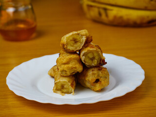 Delicious Fried slices of the ripe plantain on a white dish decorated with bananas and honey