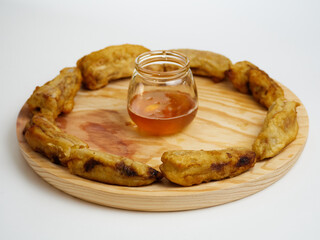 Delicious Fried slices of the ripe plantain making a circle and a glass of honey on a round wooden plate