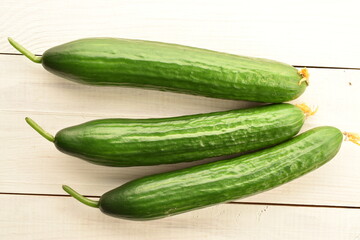 Three green cucumbers, close-up, on a wooden table, top view.