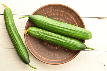 Three green cucumbers with a clay plate, close-up, on a wooden table, top view.