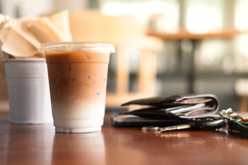 Iced coffee latte in plastic glass with men wallet and car key on wood table.