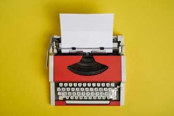 Top view of red vintage typewriter with white blank paper sheet