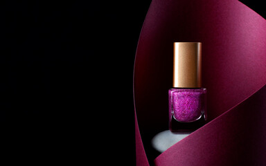 Nail polish of glittering pink color on stone inside the red paper cut against the black...