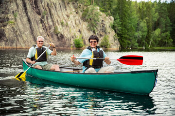 Happy mature couple in life vests canoeing in forest lake. Sunny summer day. Tourists traveling in...