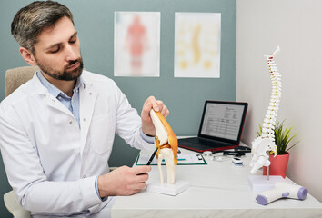 Mature doctor using a knee-joint anatomical model to analyze human knee problem areas and treatment