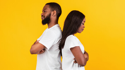 Obraz premium Black couple standing back to back, yellow studio wall