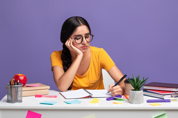 Tired indian woman sitting at desk writing in notebook