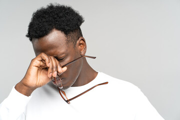 Sleepy African American man take off glasses rubbing his eyes feels tired after work on laptop computer isolated on grey background. Exhausted black male wants to sleep. Overwork, chronic fatigue eyes