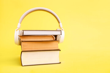 Books with white modern headphones on yellow background. Listen to the audio book concept