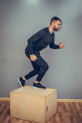 Man jumping onto the box on gray wall background. Athlete gave exercise. Jumping on the box. Phase...