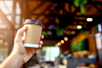 closeup hand holding paper cup of coffee in cafe with soft-focus and over light in the background
