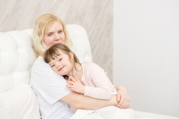 Mom hugging a girl with down syndrome at home in the bedroom on the bed. Ordinary childcare in a family for children with disabilities