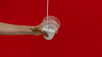 Unrecognizable woman pouring milk into glass in studio on red background. 